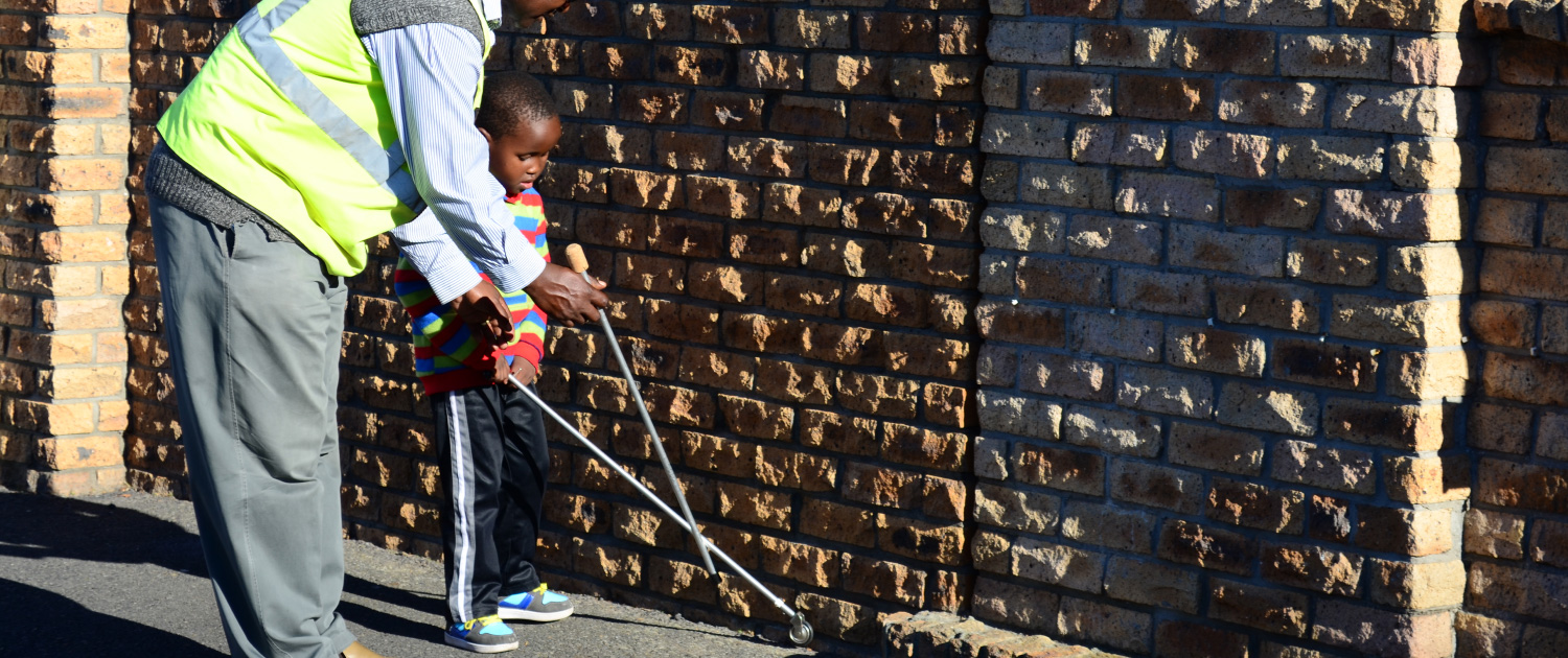 An Africane instructor shows a child how to use a white cane